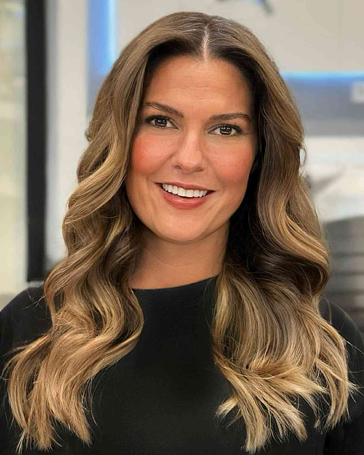 wavy blonde balayage with a center part on long hair for 40 year olds