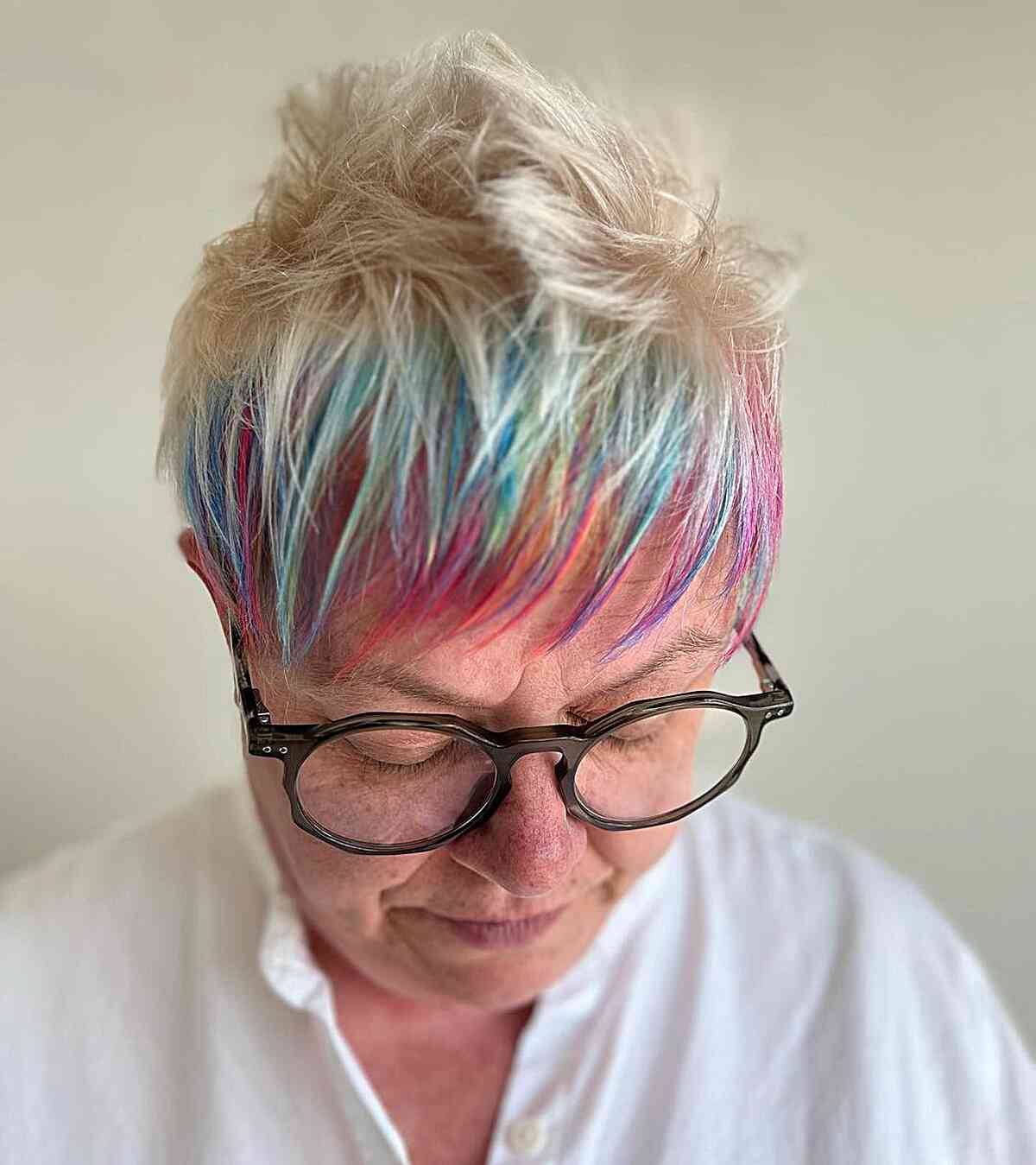 spiky blonde pixie with rainbow bangs for older women over 60 with round glasses